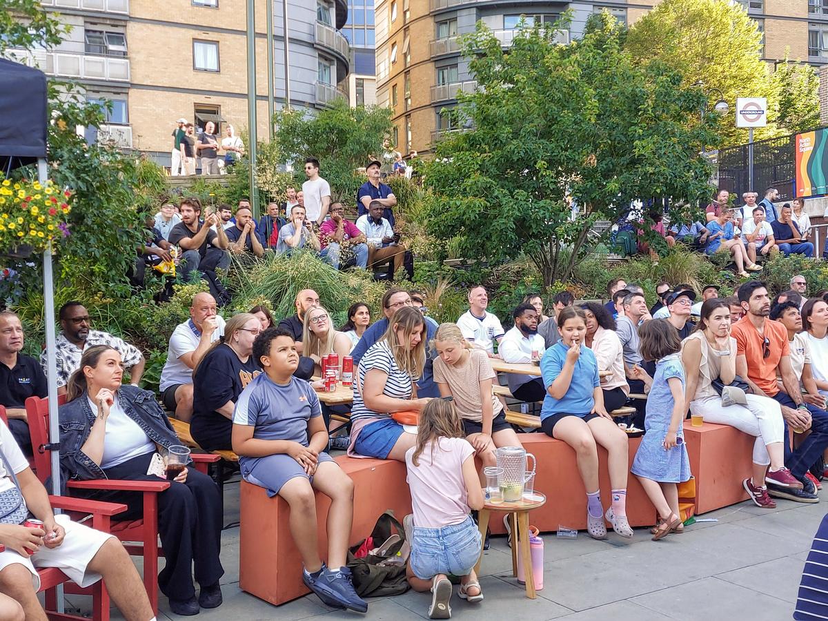 A busy summer evening on North Acton Square, people sitting on benches and crates